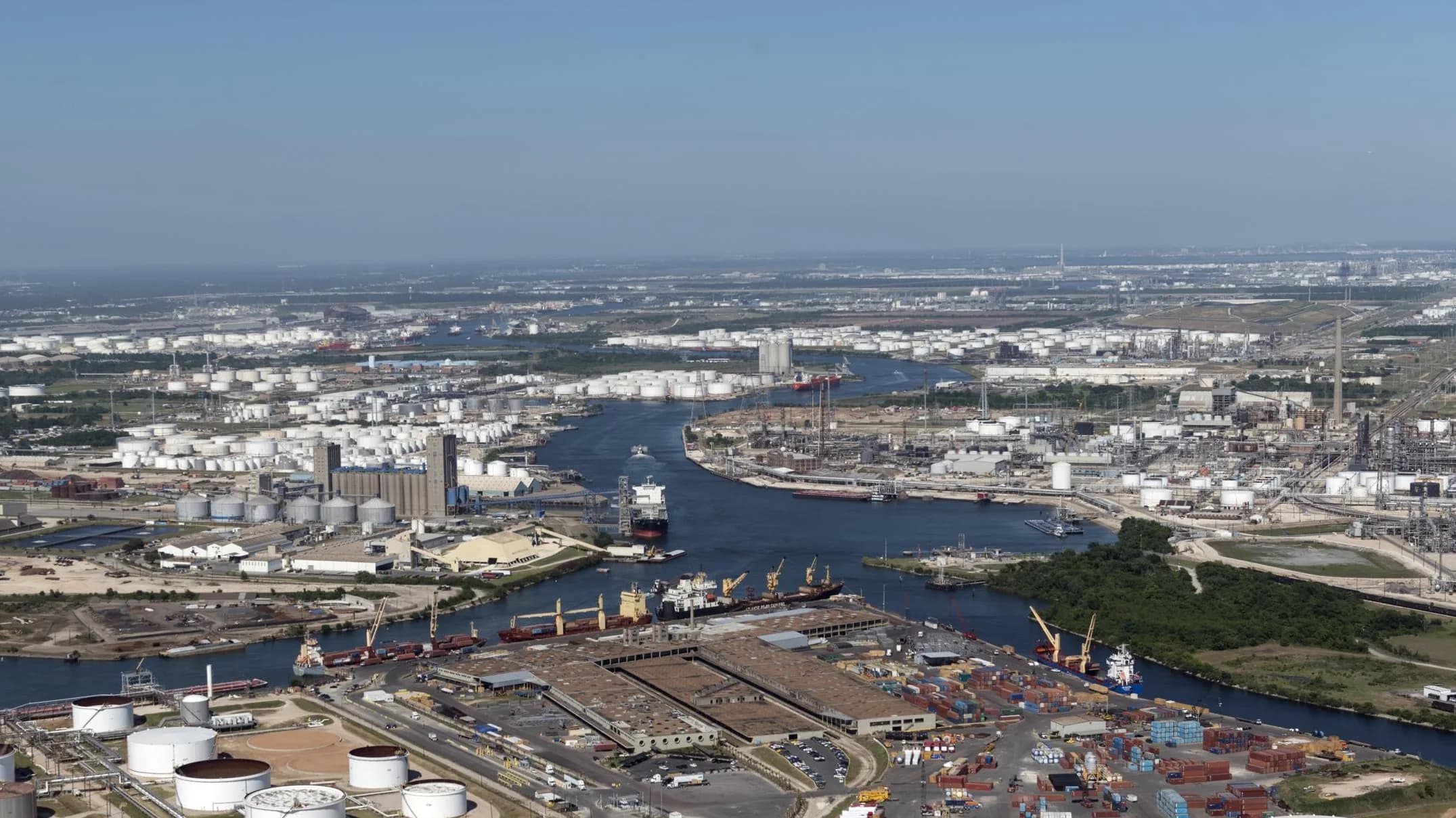 Aerial view of the Houston Ship Channel: refineries, tank farms and container terminals lining both banks, with a bulk carrier under way.