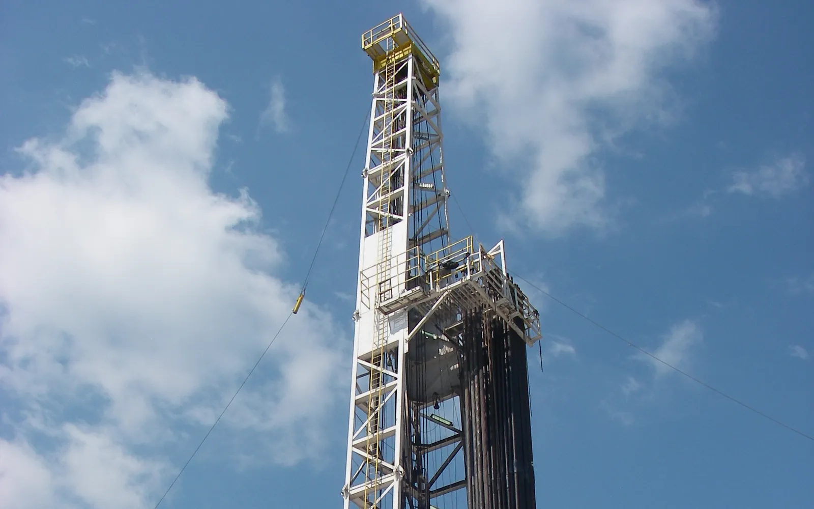 The derrick of a land drilling rig, with drill pipe racked inside it, against a blue sky in East Texas