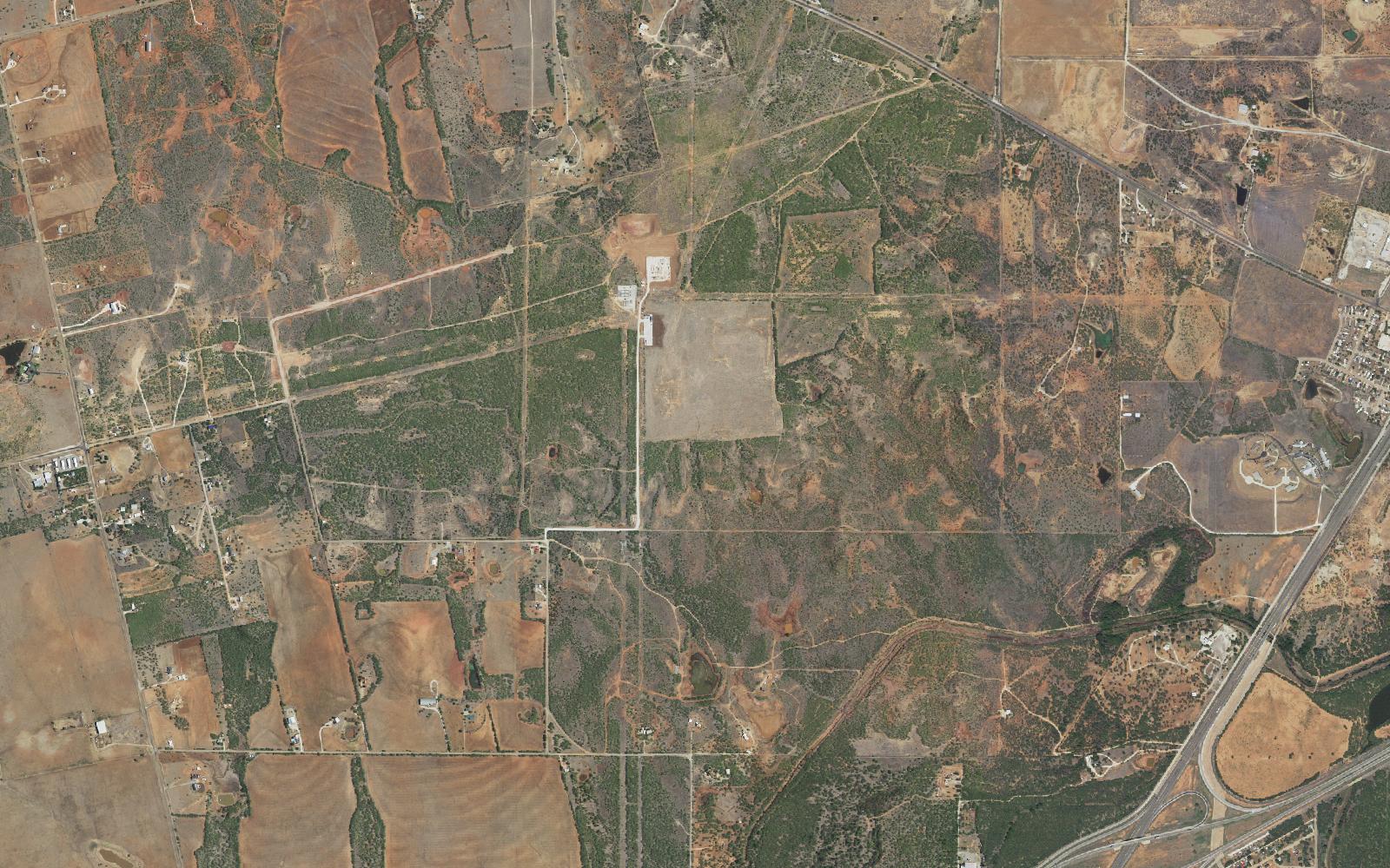 Aerial photograph of ranch land north of Abilene, Texas in July 2022: brush, pasture and dirt roads, with one bare graded pad and a small substation yard near the center.